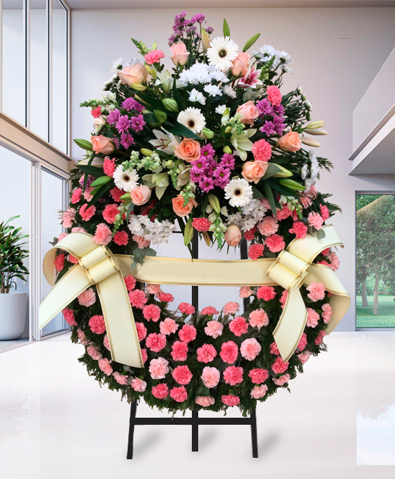 Corona funeraria de clavel rosa con centro decorado en tonos lila y coral